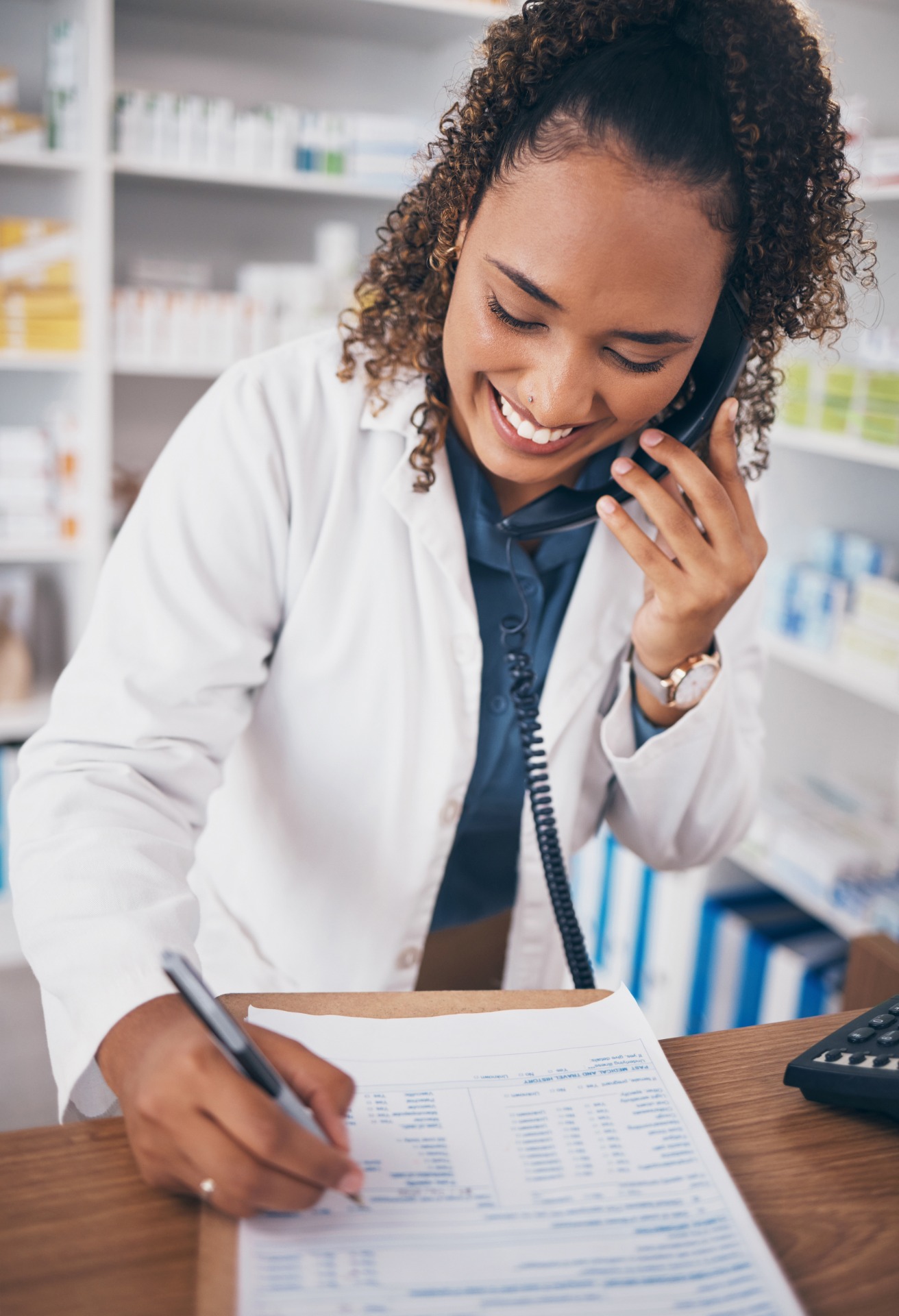 Female pharmacist smiling and on the phone while writing something on a clipboard